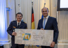 Staatsminister Albert Füracker und Präsident Ingbert Hoffmann in Polizeiuniform halten gemeinsam ein großes Schild mit dem Jubiläumslogo der Hochschule für den öffentlichen Dienst in Bayern in die Kamera.